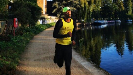 A runner in a Help Musicians vest running next to a canal